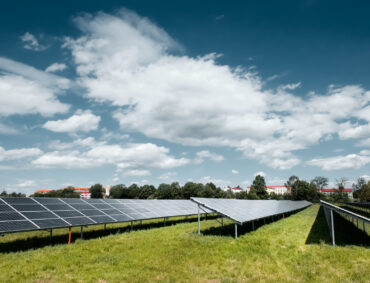 Solar power plant, blue solar panels on orange Autumn grass field under blue sky with clouds. Toned panoramic image. Solar power generation, renewable energy production