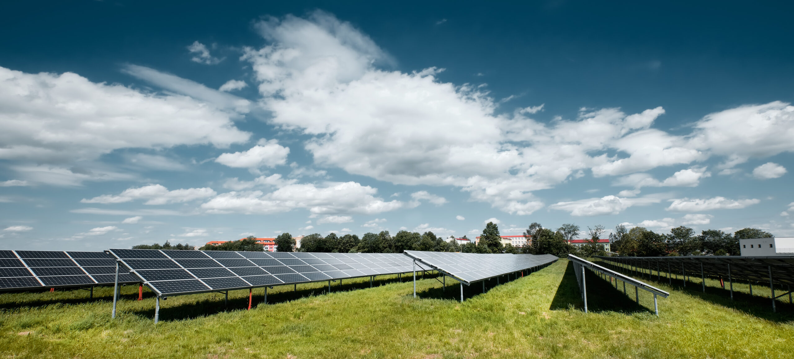 Solar power plant, blue solar panels on orange Autumn grass field under blue sky with clouds. Toned panoramic image. Solar power generation, renewable energy production